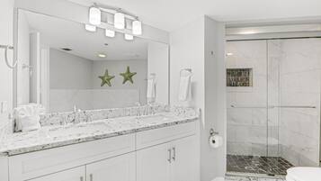 A modern bathroom with a large mirror, white vanity, and a shower area.
