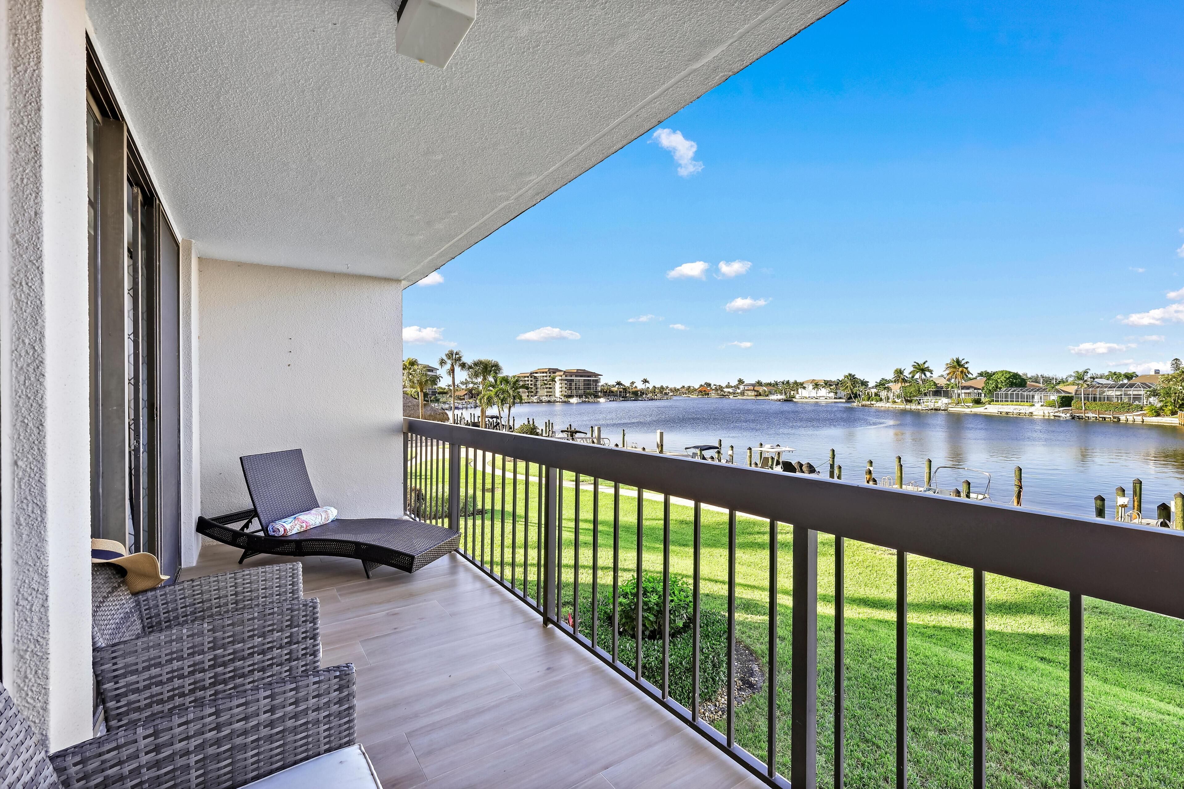 A balcony with a view of a lake, a lounge chair, and a small table.