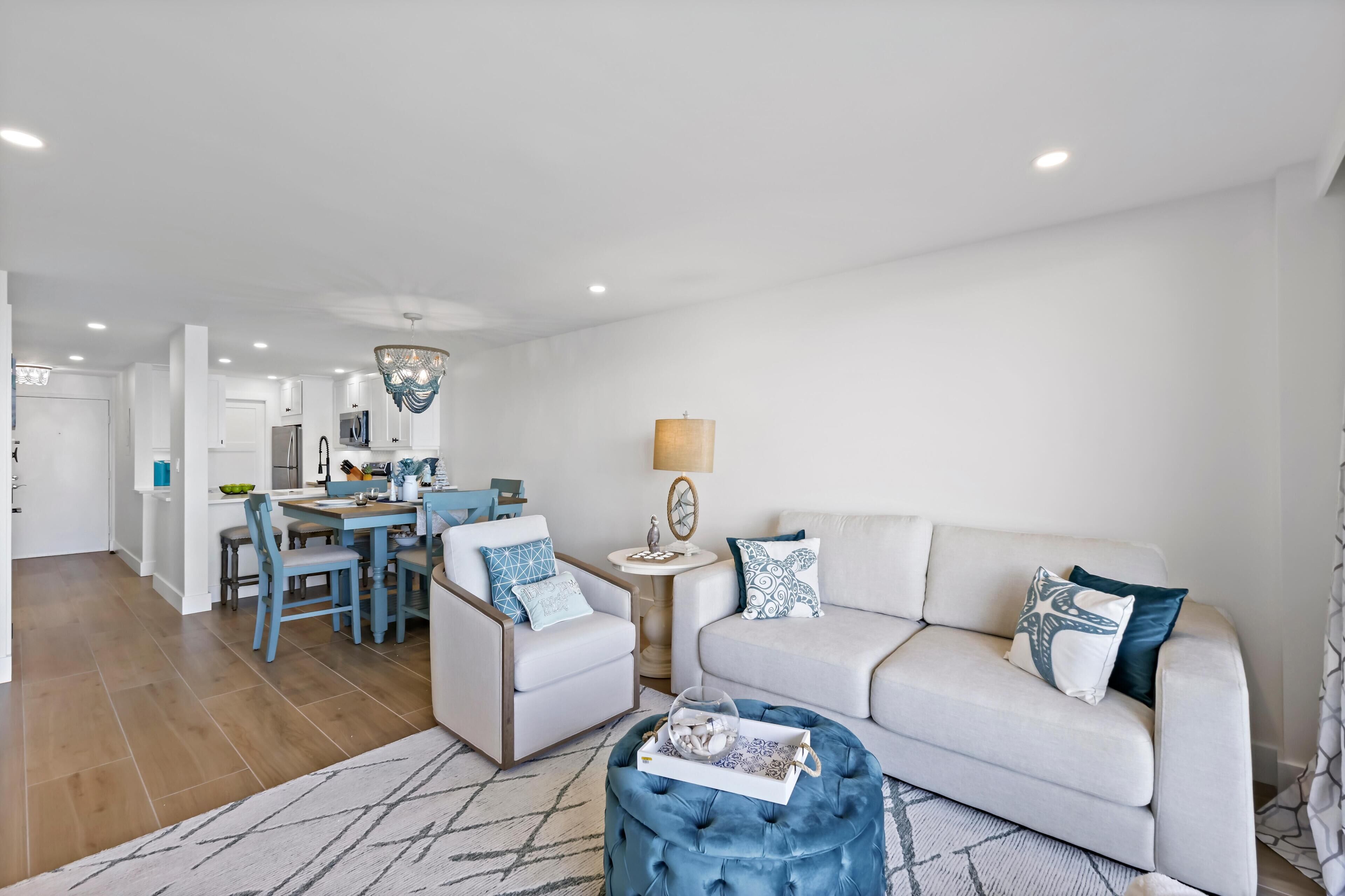A modern living room with a sofa, armchairs, a dining table, and a kitchen in the background.