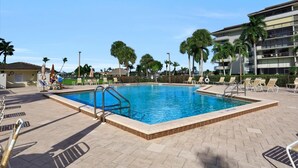 Une piscine rectangulaire, bordée d’une terrasse carrelée et entourée de chaises longues et de palmiers.