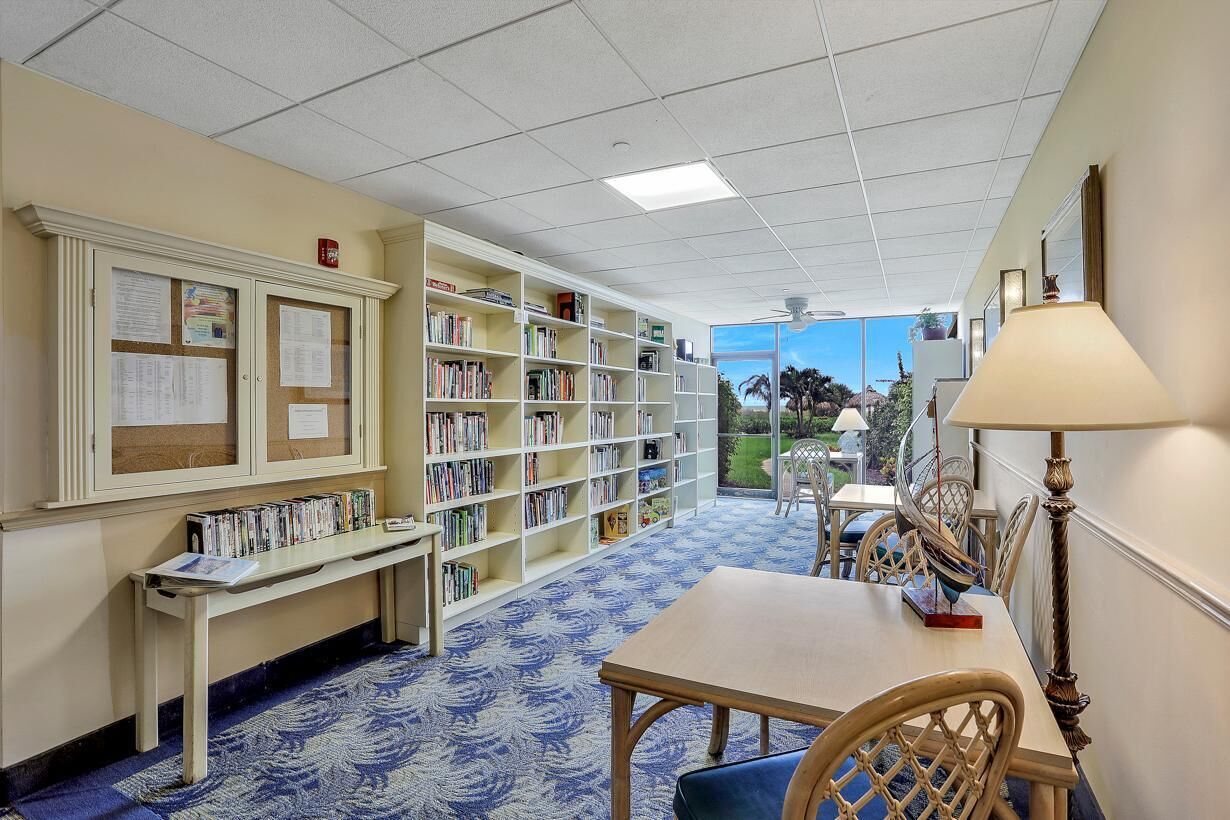 A library with bookshelves, a table, chairs, and a view of the outdoors.