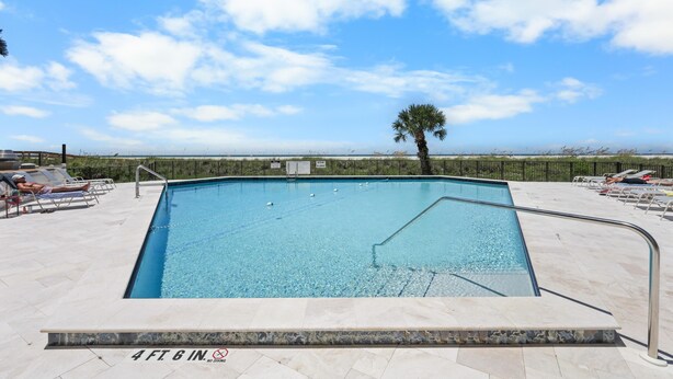 A rectangular swimming pool with a 4 ft 6 in depth marker, surrounded by lounge chairs and a palm tree. - Tradewinds 701 (Marco Island)