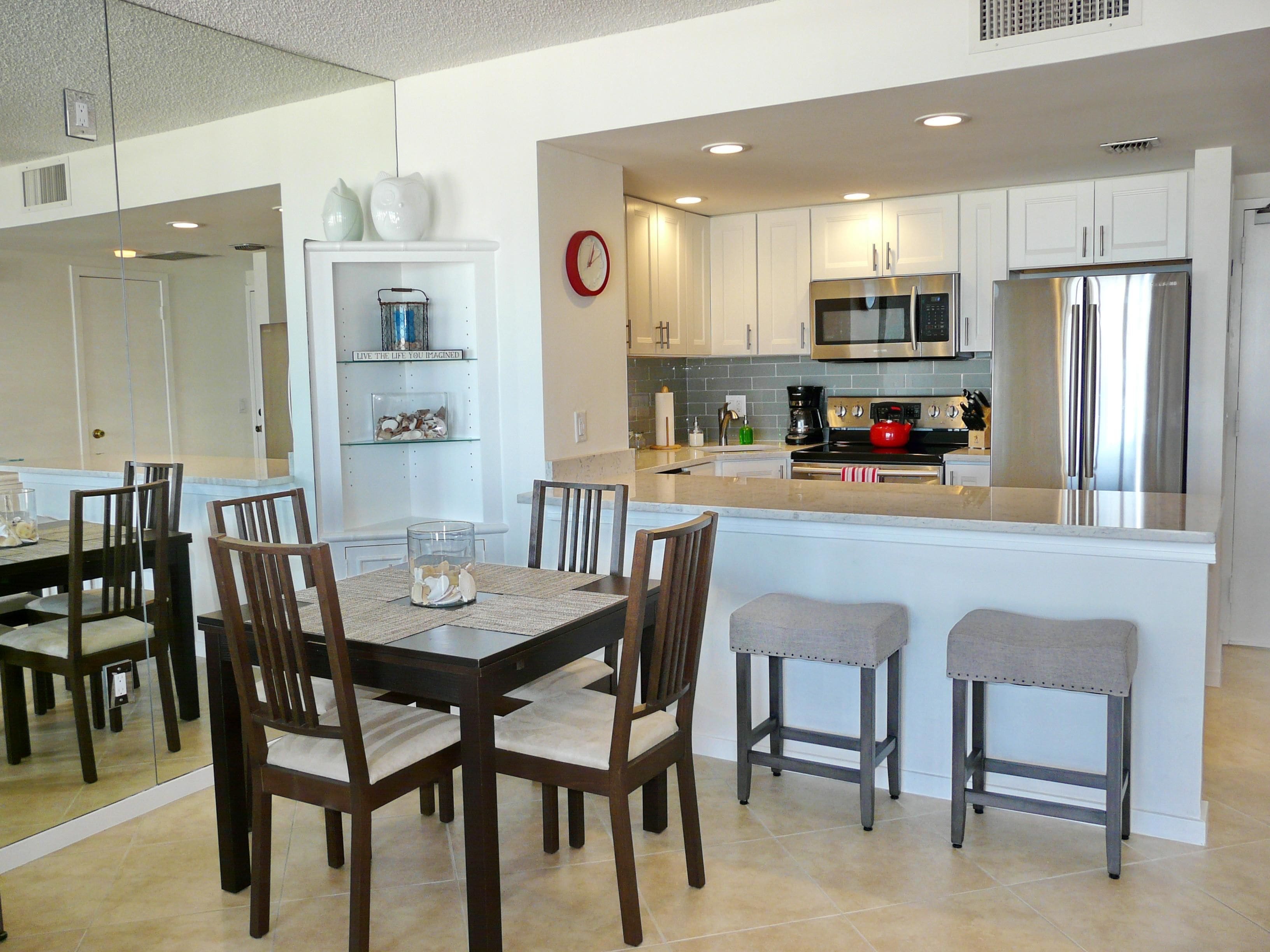 A modern kitchen with white cabinets, stainless steel appliances, and a dining area with wooden chairs and a glass table.