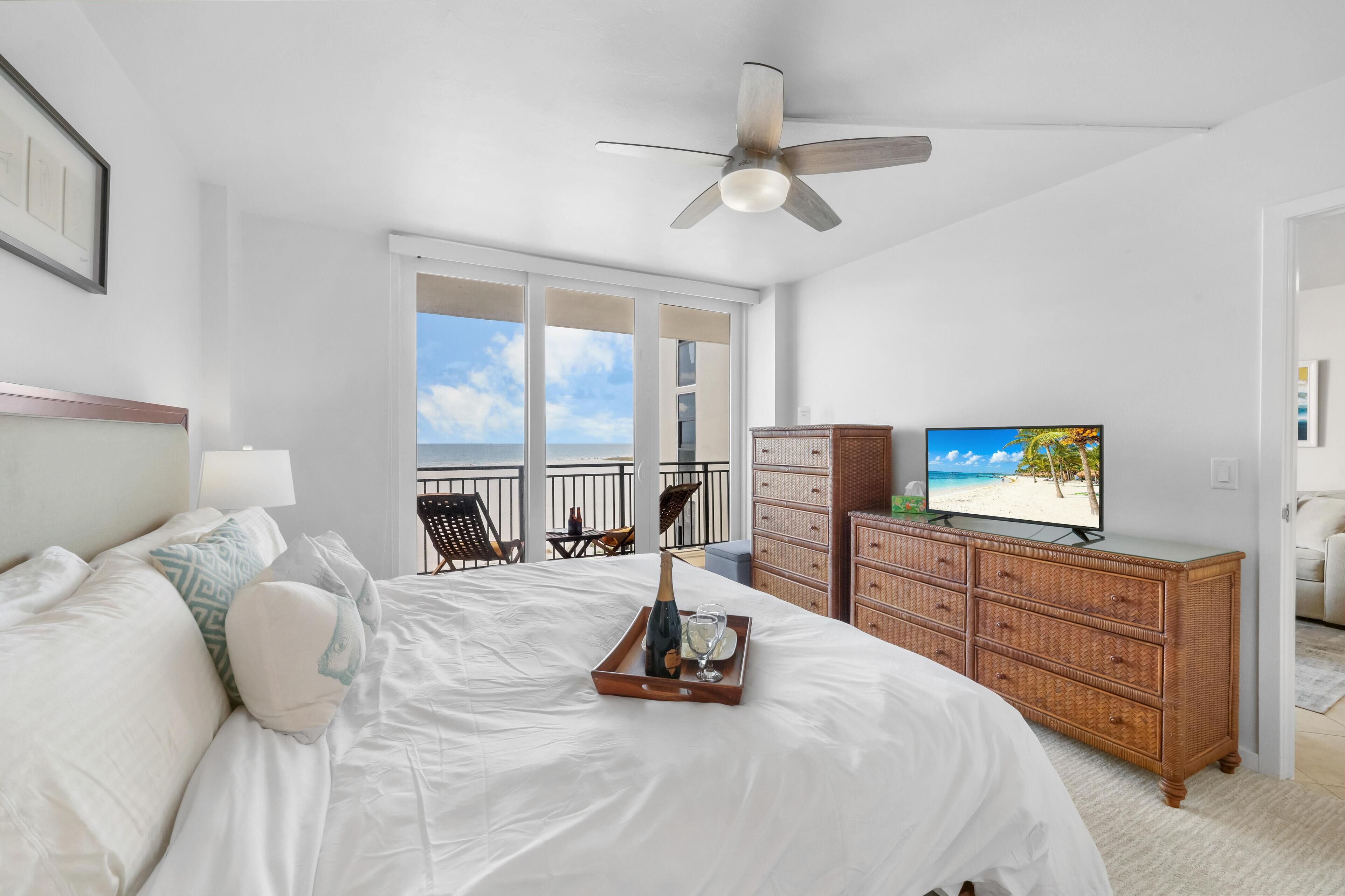 Habitación de hotel con cama, cómoda, televisión y balcón con vista al océano.