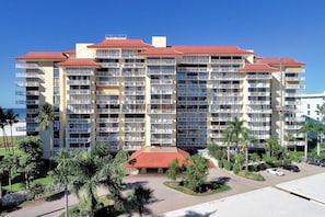 A multi-story hotel with balconies, a red roof, and a landscaped courtyard with palm trees.