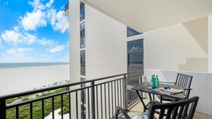 A balcony with a view of the beach, a table with chairs, and a railing. - Tradewinds 701 (Marco Island)