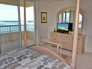 Un dormitorio con cama, cómoda, televisor y balcón con vistas al mar.