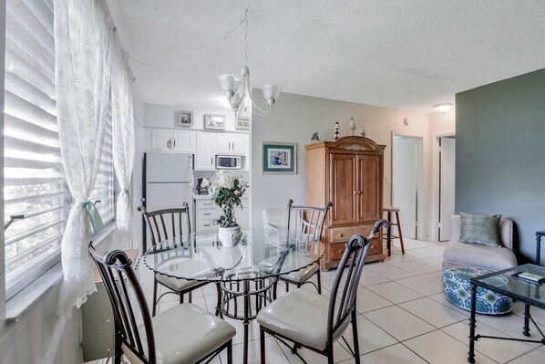 A dining area with a glass table surrounded by chairs, a wooden cabinet, and a microwave in the background. - Idyllic Condo With Brief Walk to Beach and Restaurants (Marco Island)