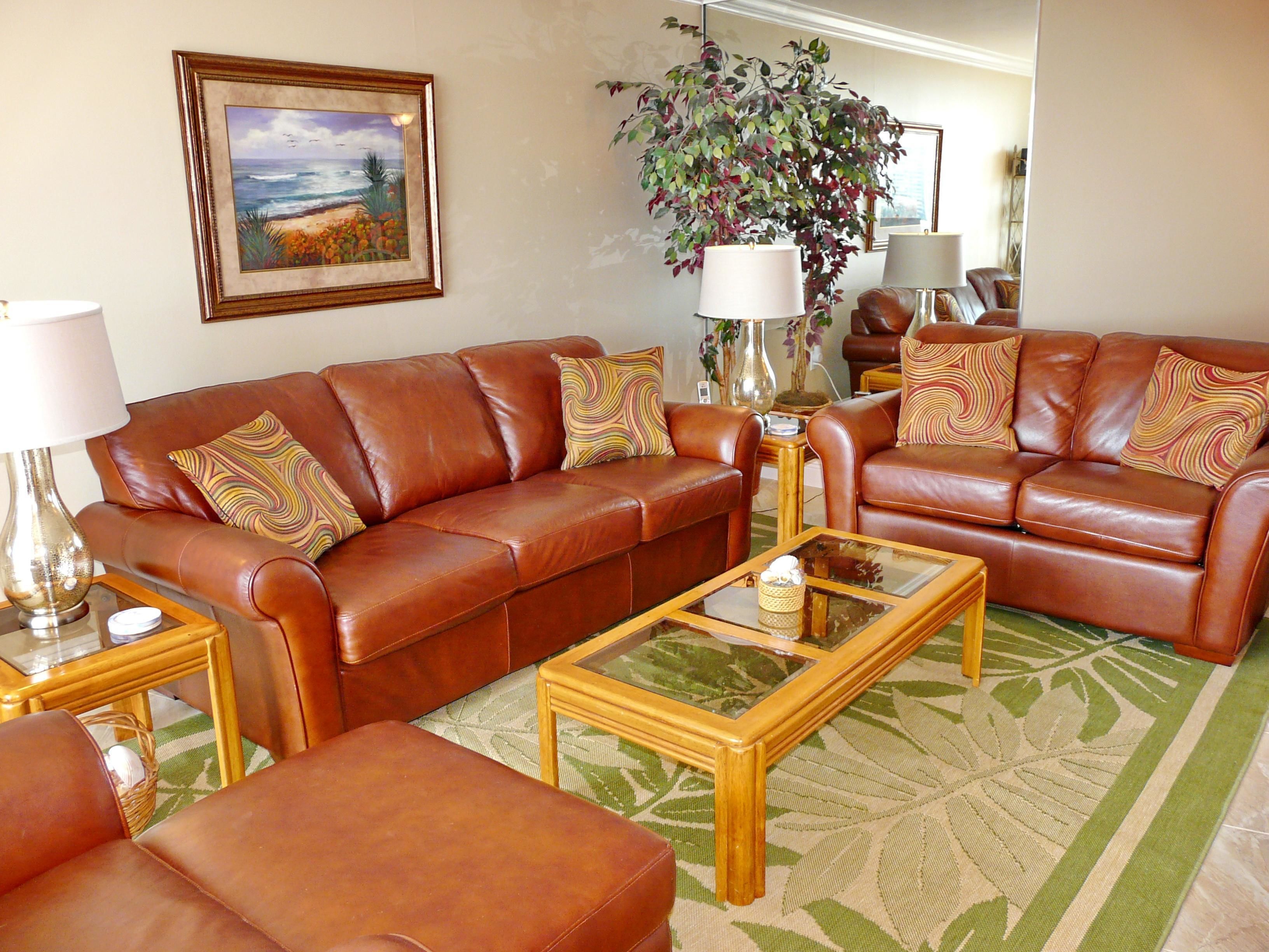 A living room with two brown leather sofas, a glass coffee table, and a green patterned rug.