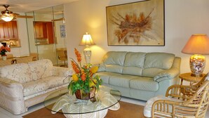 En stue med sofa, sofabord med blomster, lampe og stol.
