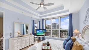 A bedroom with a bed, a television, a dresser, and a window with a view of buildings. - Spacious Condo With sky Views and Steps to South Beach (Marco Island)