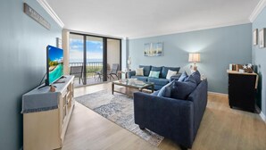 A modern living room with a sofa, a coffee table, a TV, and a balcony with a view. - Beachfront Condo With Pool and Balcony Facing Beach (Marco Island)
