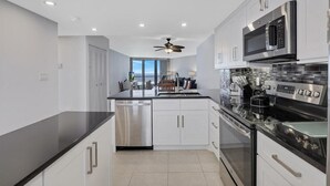 A modern kitchen with white cabinets, stainless steel appliances, and a black countertop. - Beachfront Condo With Pool and Balcony Facing Beach (Marco Island)