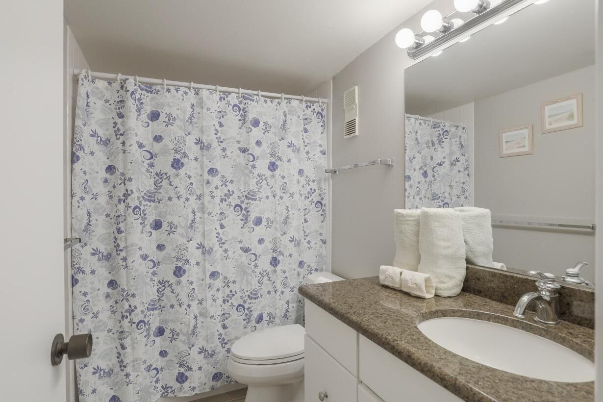 A bathroom with a shower curtain, toilet, sink, and mirror.