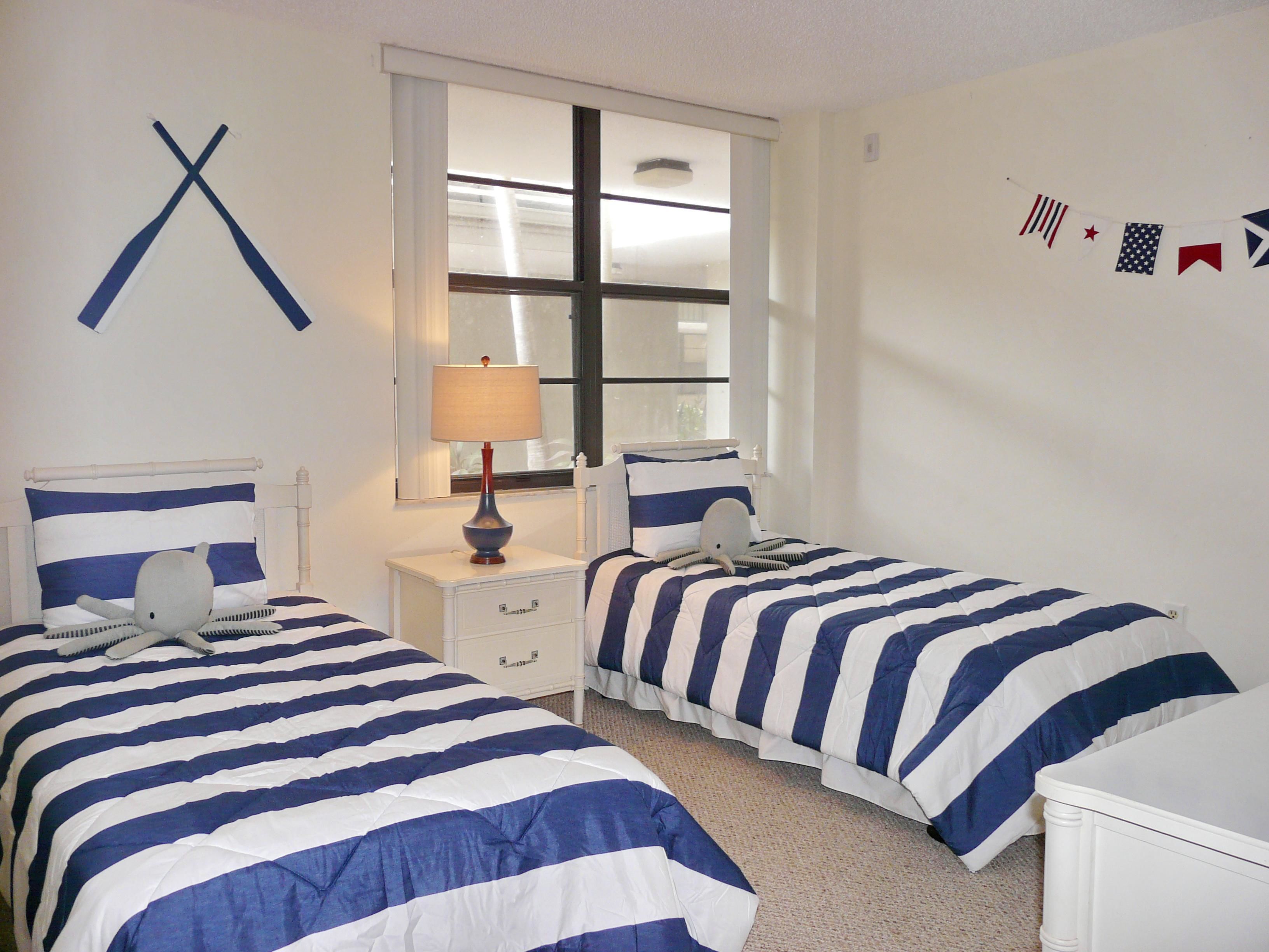 Quarto com duas camas, uma janela, um abajur e um objeto decorativo na parede.