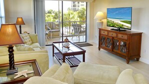 A living room with a sofa, armchairs, a coffee table, a TV, and a balcony with outdoor furniture. - Bright Condo in Community With Pool/steps to Beach (Marco Island)
