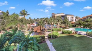 A resort with a swimming pool, palm trees, and a thatched-roof structure. - Bright Condo in Community With Pool/steps to Beach (Marco Island)