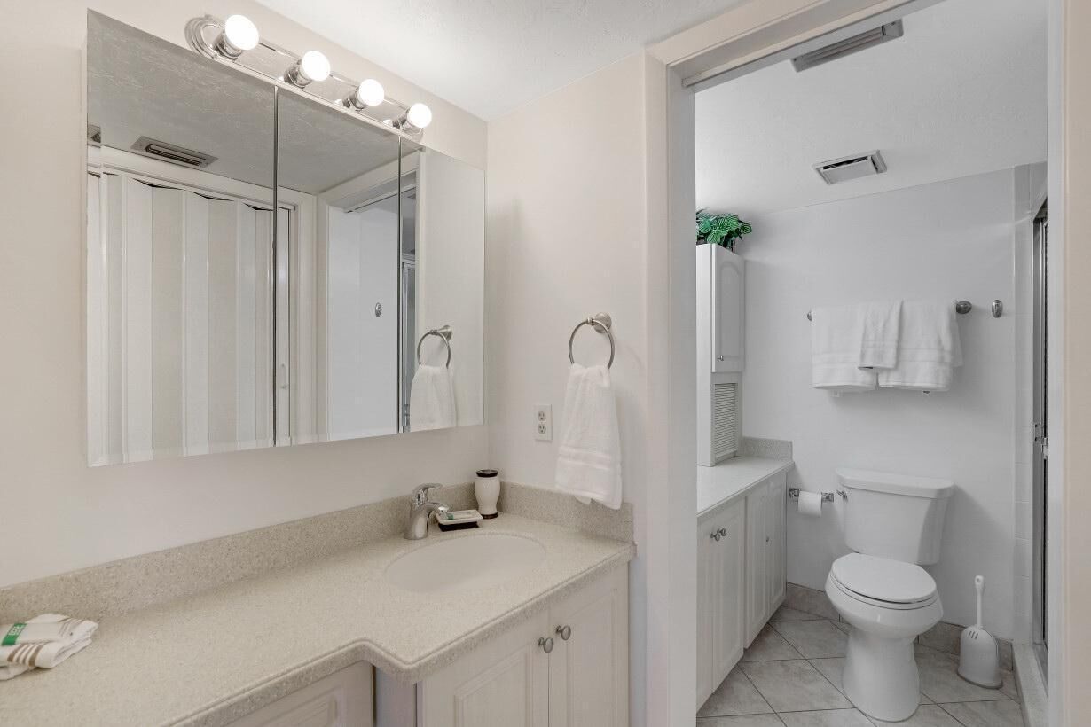 A modern bathroom with a large mirror, vanity, toilet, and shower.