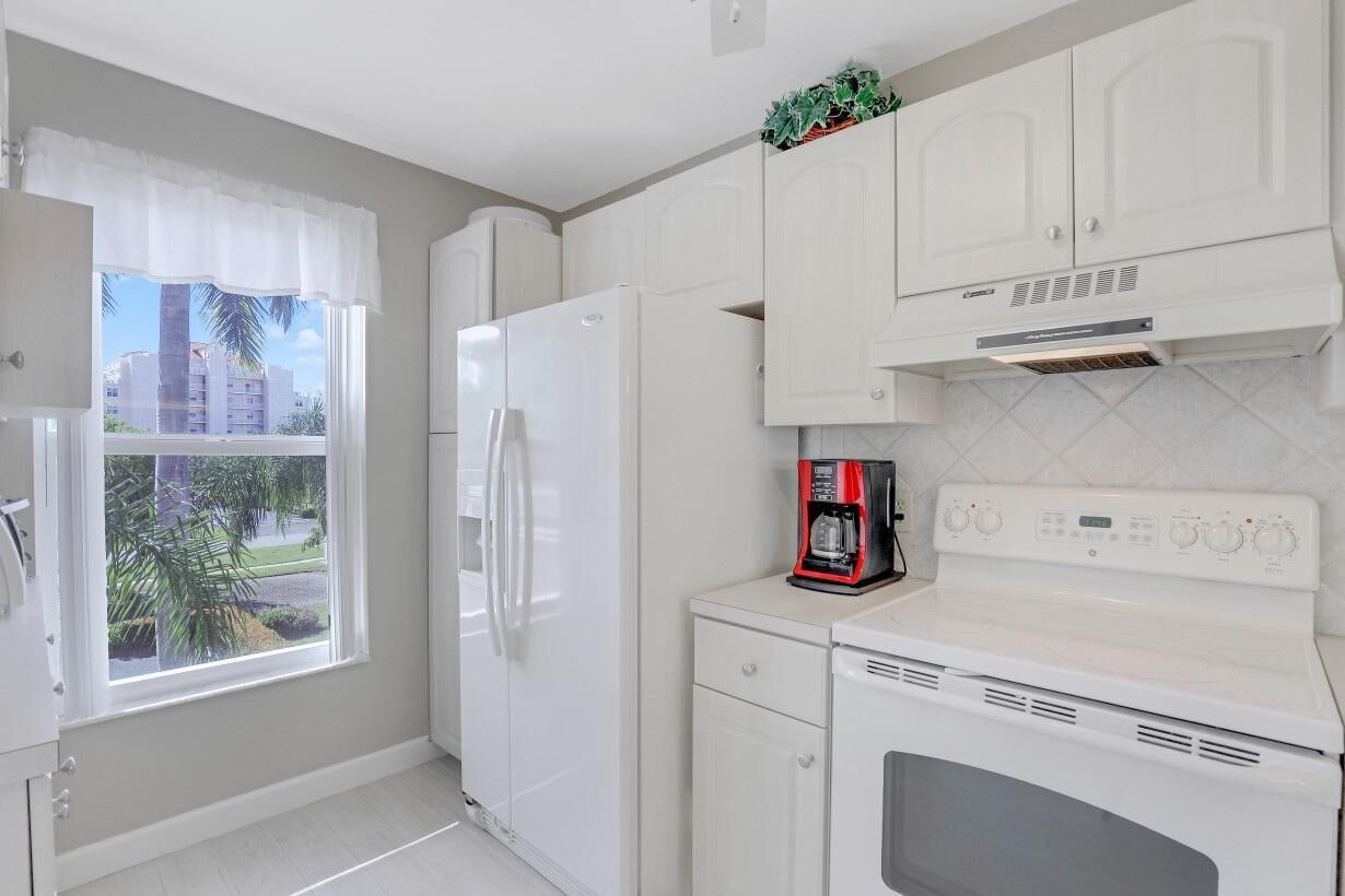 A kitchen with white cabinets, a refrigerator, a coffee maker, and a stove.