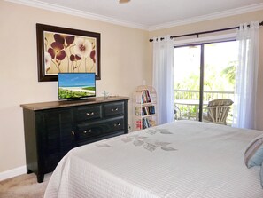 A bedroom with a bed, a dresser, a television, a bookshelf, and a balcony with a chair. - Bright Condo in Community With Pool/steps to Beach (Marco Island)