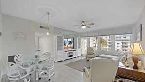 Un salon moderne avec une table à manger en verre, des chaises blanches, un canapé et un téléviseur.