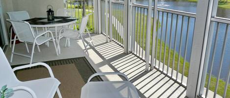 Uma varanda com cadeiras brancas, uma mesa e vista para um lago e edifícios.