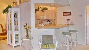 A compact kitchen with white cabinets, a microwave, and a small bar area with stools. - Quiet, Gated Community With Pool and Tennis Courts (Marco Island)