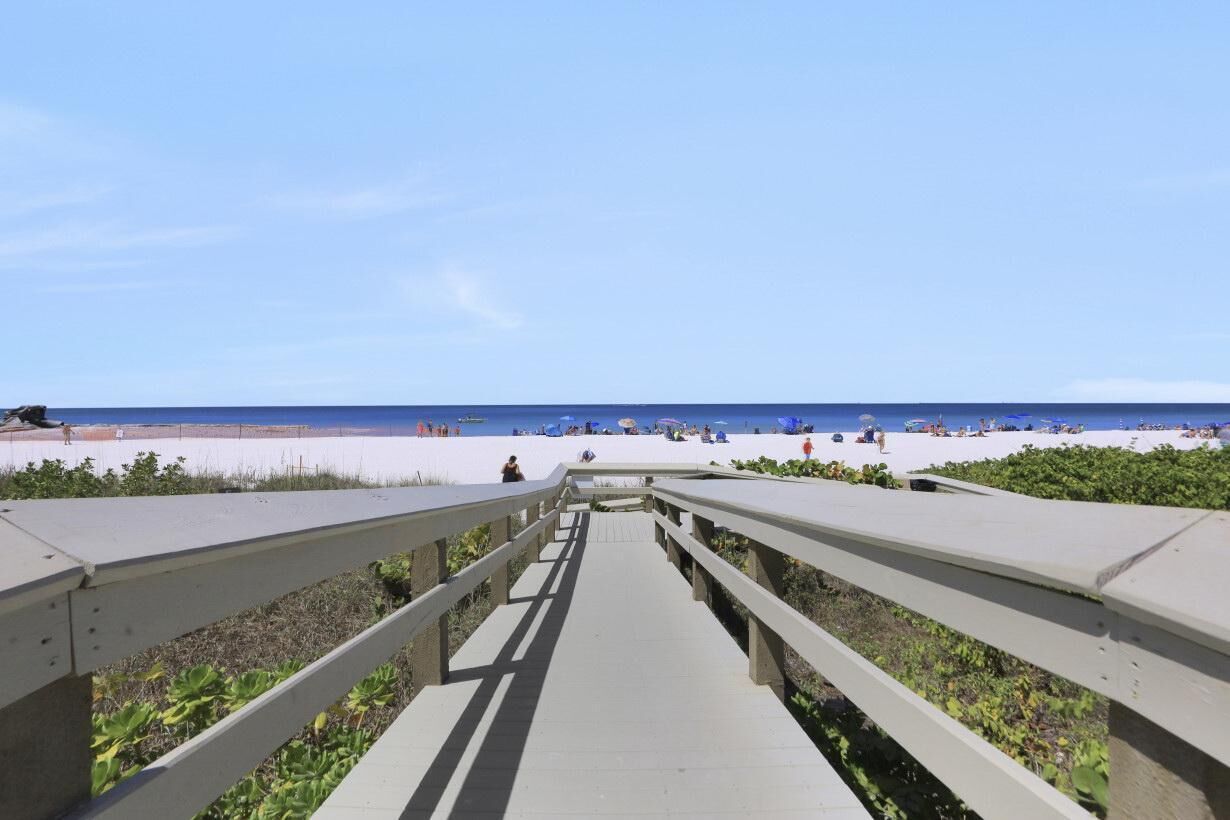 A beach pathway leading to a sandy beach with people and umbrellas.