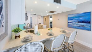 A modern kitchen with a central island, white cabinetry, and a dining area with wicker chairs.