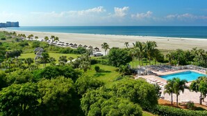 A resort with a pool, beach, and lush greenery.
