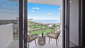 A balcony with wicker chairs and a small table, overlooking a beach and golf course.