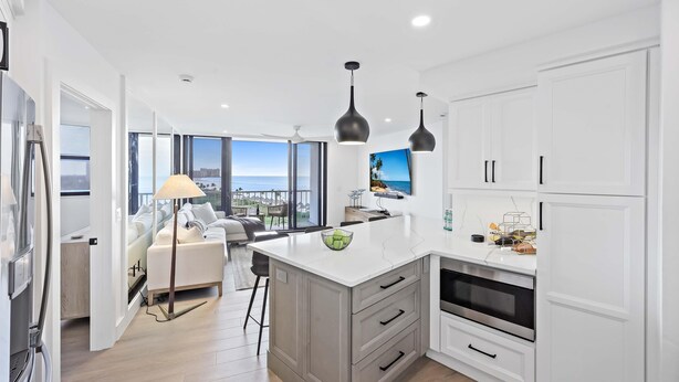 A modern kitchen with white cabinets, a large island, and a view of the ocean.