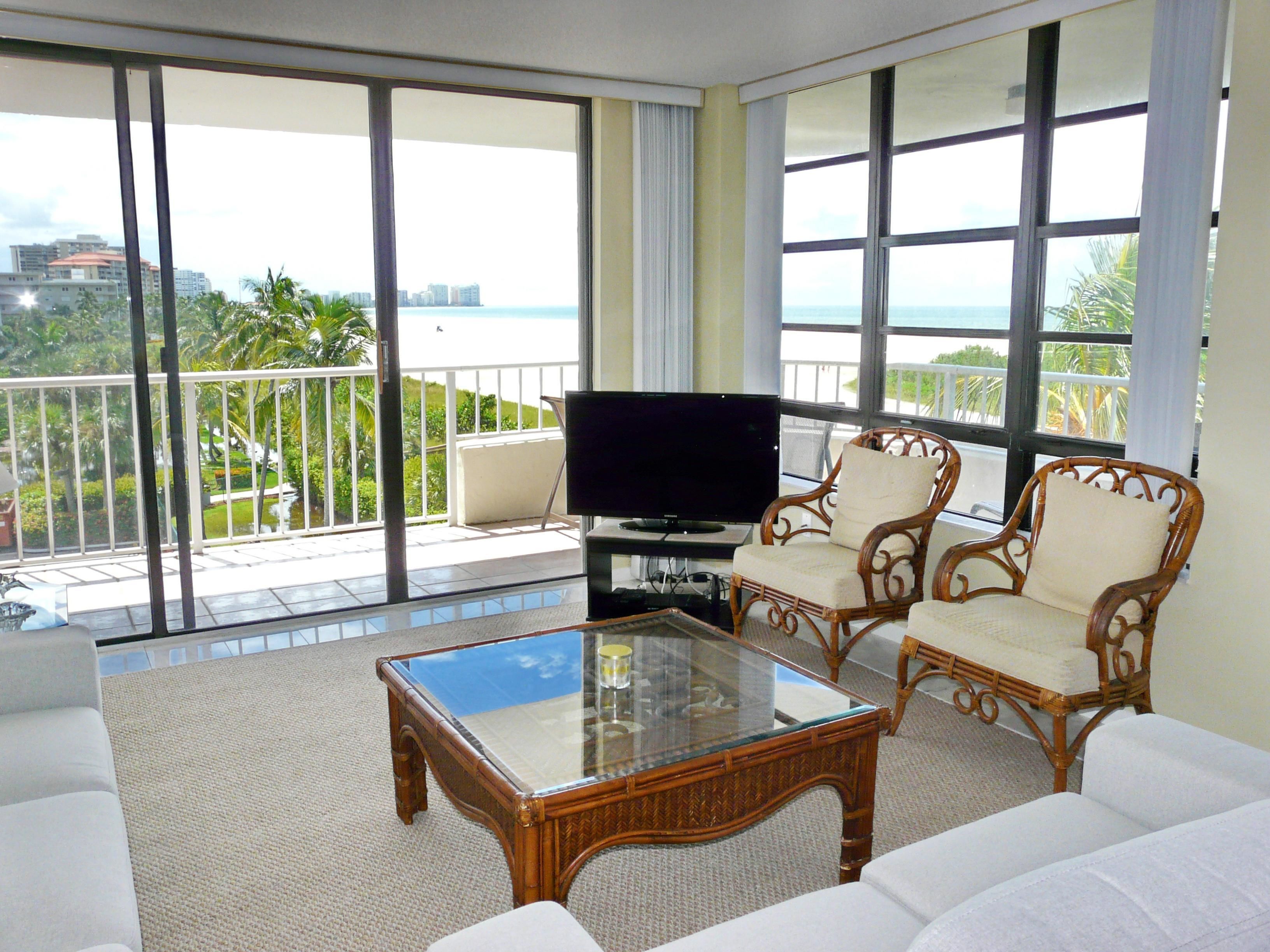 A spacious balcony with a glass coffee table, wicker chairs, and a flat-screen TV.