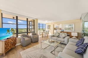 A spacious living area with a flat-screen TV, comfortable seating, a dining area, and a kitchen. - Front Unit Facing Beach With Wraparound Balcony (Marco Island)