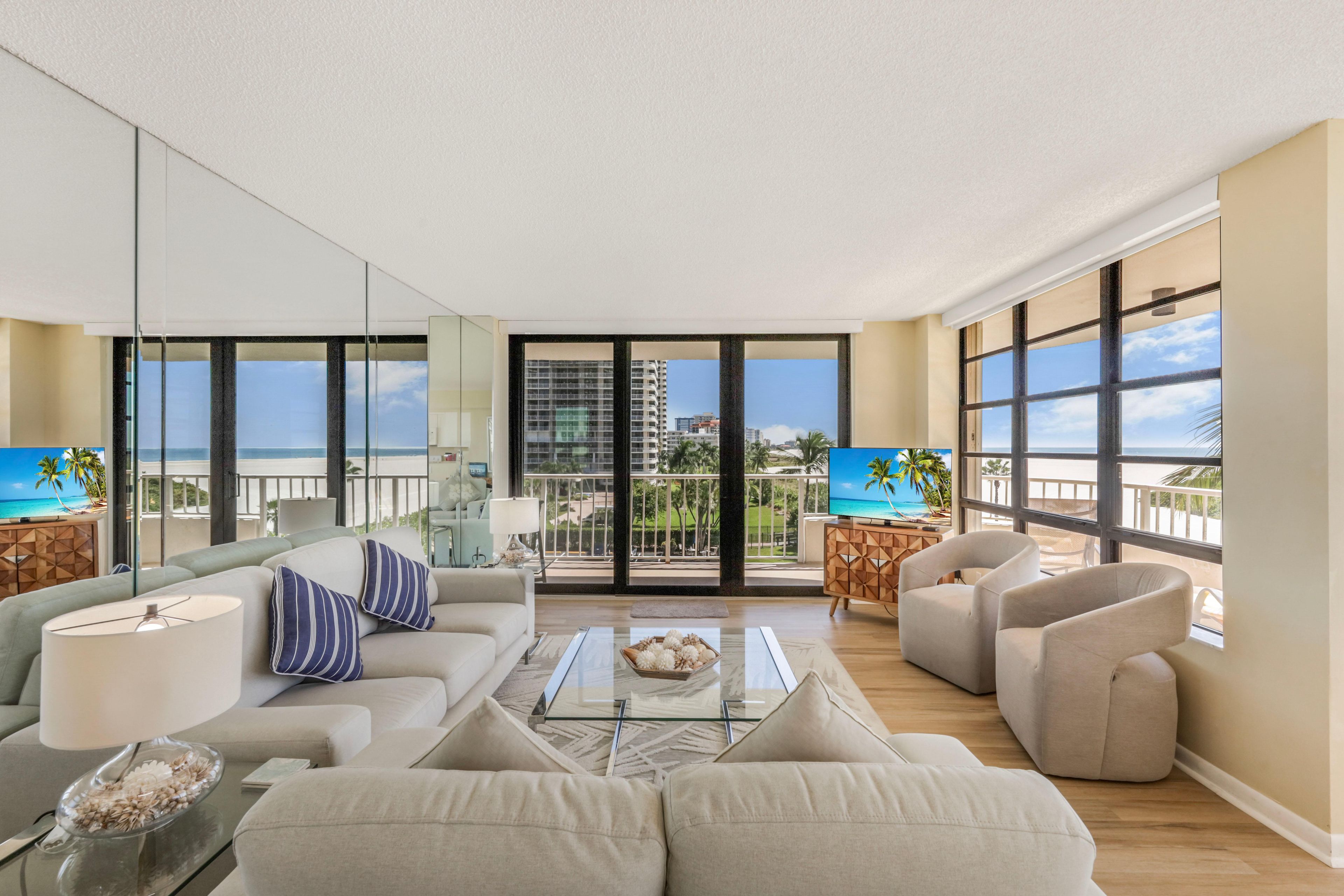 A spacious living room with a balcony, large windows, and a view of the ocean.