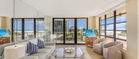 A spacious living room with a balcony, large windows, and a view of the ocean.