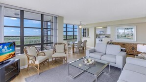 A spacious living room with large windows, a dining area, and a kitchen.