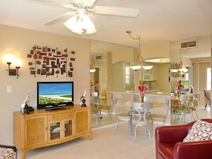 A living room with a TV, wooden cabinet, red sofa, and a dining area with chairs and a table.