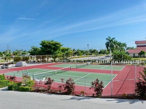 A tennis court with a net, surrounded by greenery and a building in the background.