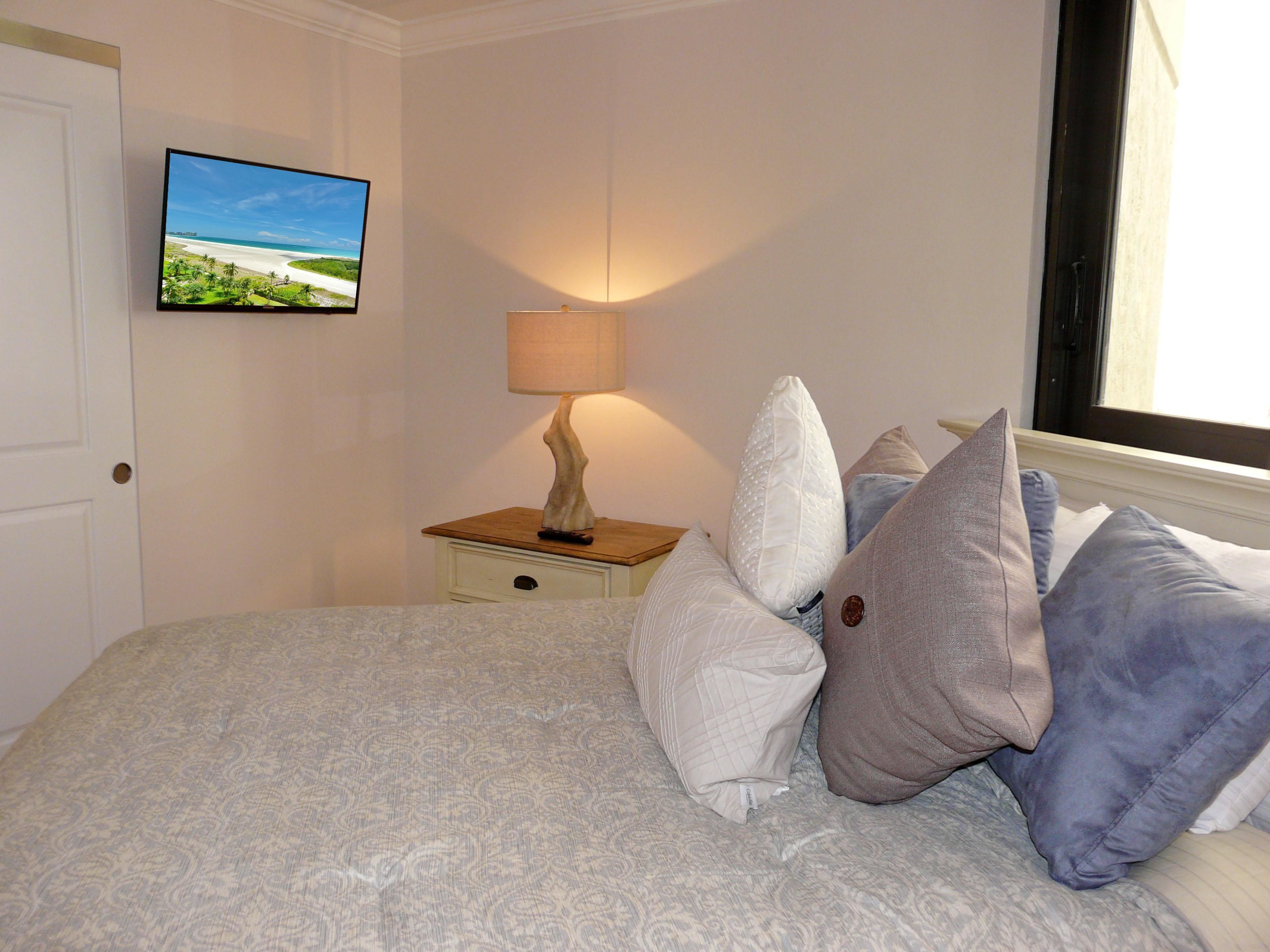 A neatly made bed with patterned bedding, a bedside lamp, and a television displaying a beach scene.