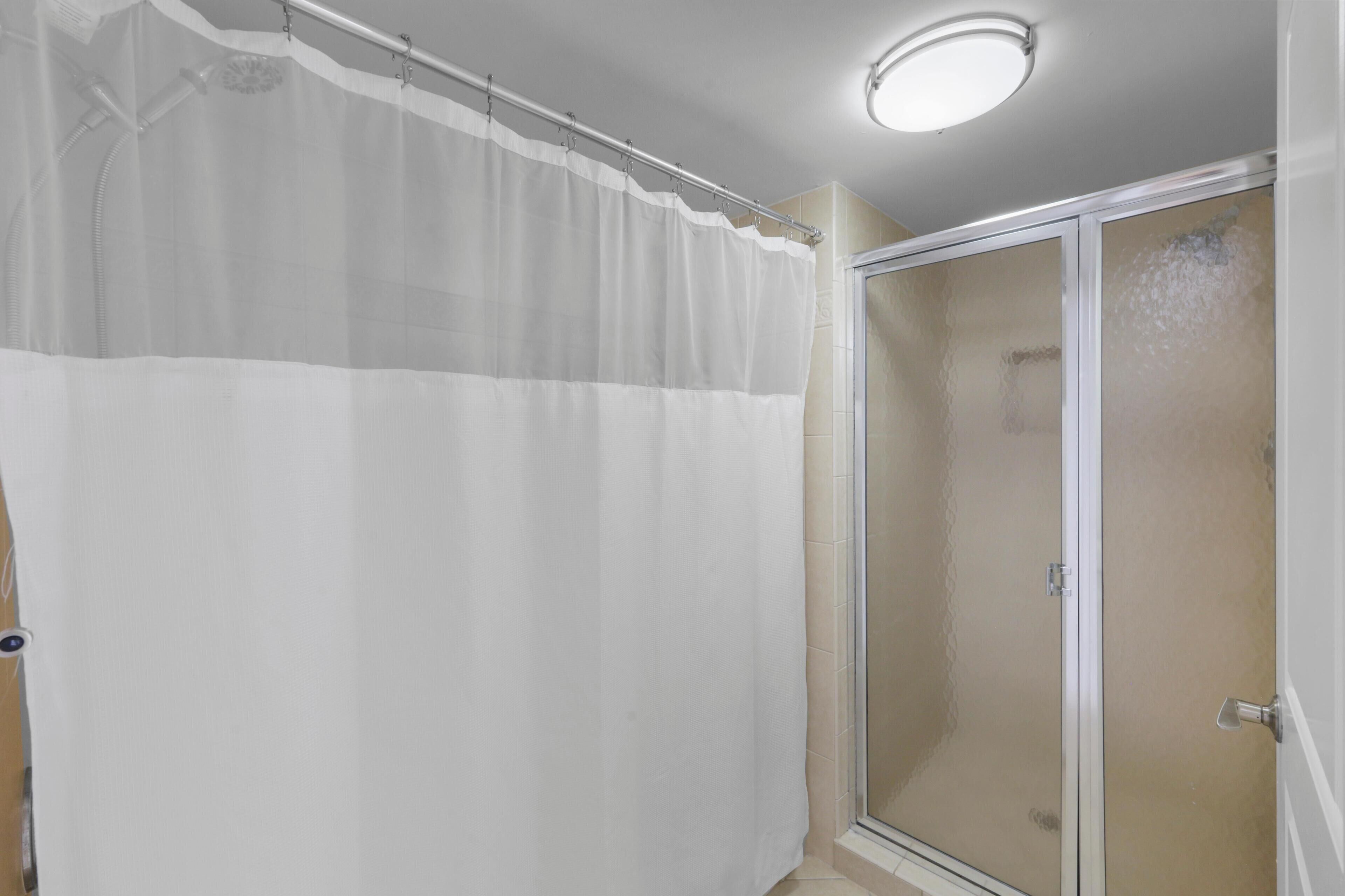 A shower area with a glass door and a white shower curtain.