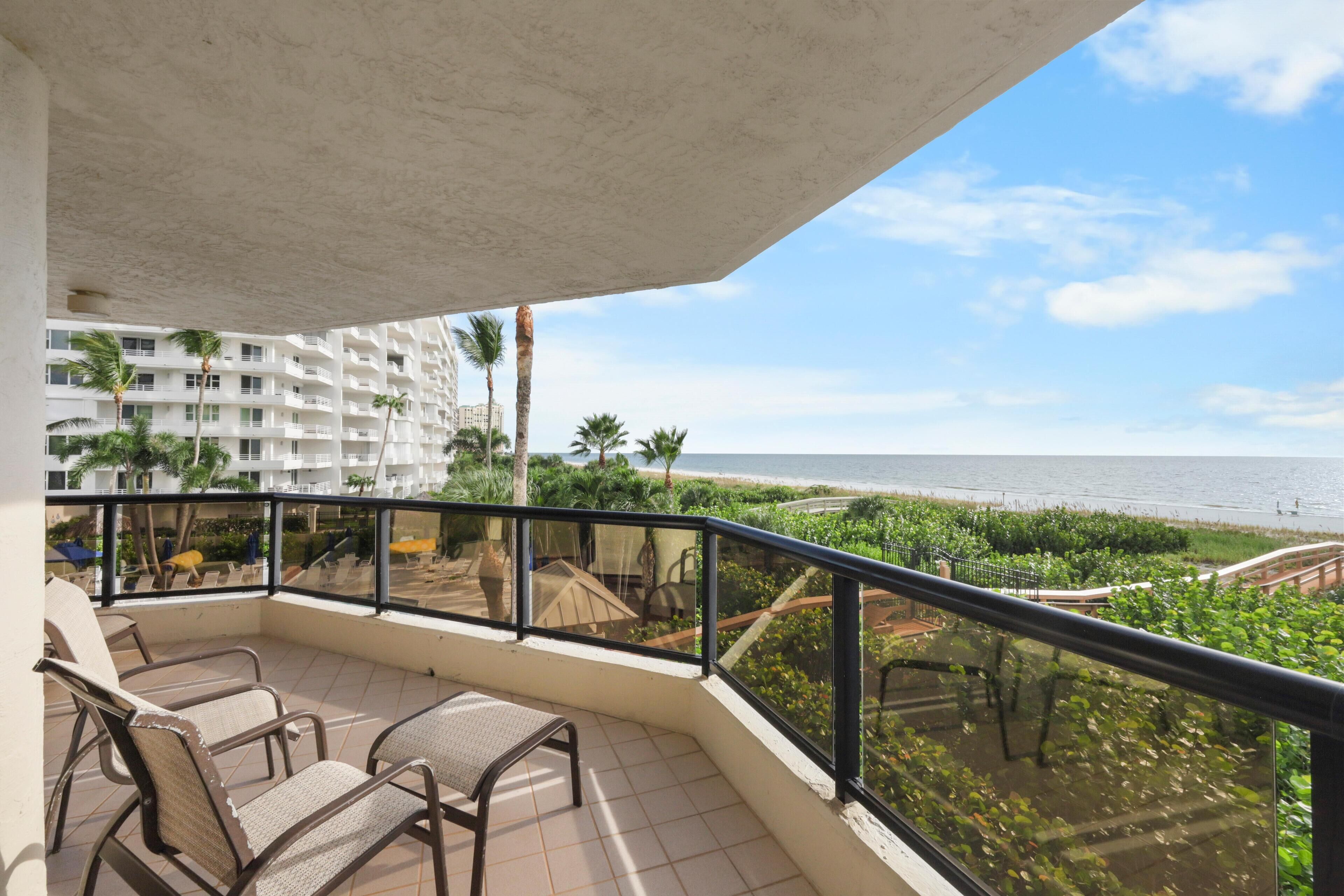 Un balcon avec des chaises, une vue sur la plage et un palmier.