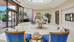 A spacious lobby with a central round table, blue upholstered chairs, and a glass entrance.