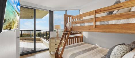 A bedroom with a wooden bunk bed, a large window with a view of a balcony, and a nightstand with a lamp.