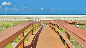 Une promenade en bois menant à une plage, avec un ciel dégagé.