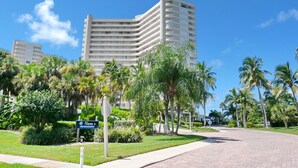 A modern hotel with a curved facade, surrounded by lush greenery and palm trees. - Eye-catching Beachfront Condo With Pool and Nice Views (Marco Island)