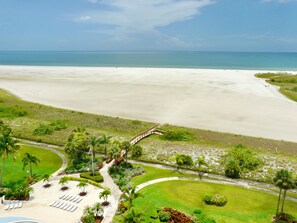A resort with a beach view, a pool, and a landscaped garden with palm trees. - Eye-catching Beachfront Condo With Pool and Nice Views (Marco Island)