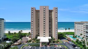 A tall hotel with a central courtyard, a beach view, and a parking area. - Inviting Beachfront Condo With Pool, spa and Views (Marco Island)