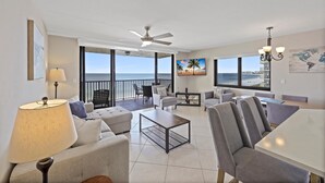 A spacious living area with a balcony overlooking the ocean, furnished with a sofa, chairs, and a coffee table. - Inviting Beachfront Condo With Pool, spa and Views (Marco Island)