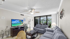 A living room with a television, grey sofa, and a ceiling fan. - Stylish Condo Across From South Beach (Marco Island)